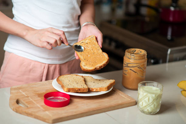 frau macht erdnussbutter und bananen-sandwich zum frühstück mit avocado-smoothie - butter bread breakfast table stock-fotos und bilder