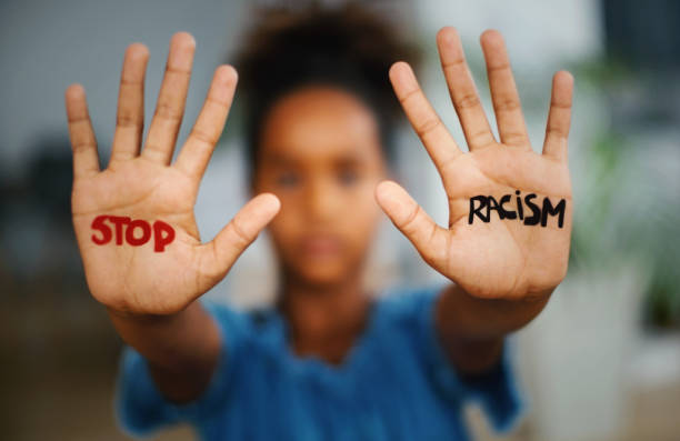 Stop racism. African american girl  standing indoors and looking at the camera. She's showing an message that says Stop Racism on her hands. palm of hand photos stock pictures, royalty-free photos & images