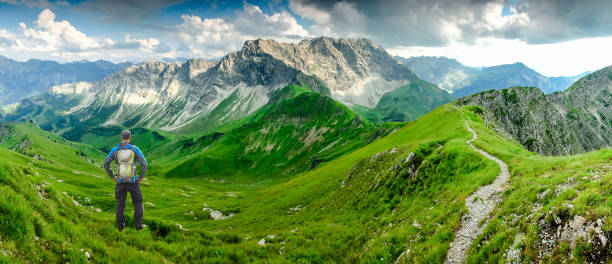 wanderer man auf wanderweg mit rucksack entspannt stehend und genießen panoramablick auf die berge. alpen, hohe gänge, allgäu, bad hindelang, hinterstein, bayern, deutschland. - allgau field landscape bavaria stock-fotos und bilder