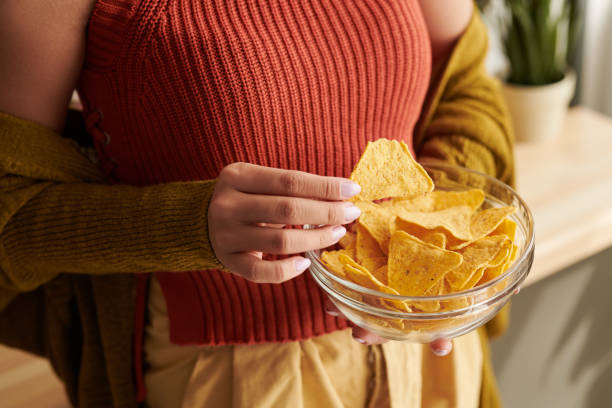 Close-up of unrecognizable woman in bright top and cardigan eating nachos from bowl at home, unhealthy food concept Eating nachos from bowl tortilla chip photos stock pictures, royalty-free photos & images