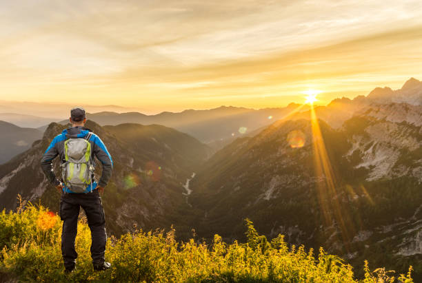 istock Man reaching summit enjoying amazing sunrise in the mountains. Backlight Sunlight with beautiful lens flares and sunbeams. Julian Alps, Triglav National Park, Slovenia, Mountain Slemenova, Sleme. 1254980583