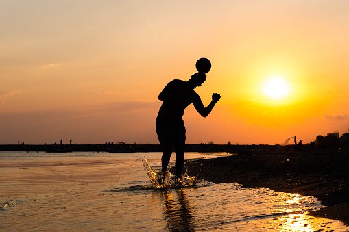 silhouette of adult male playing football at the beach against sunset