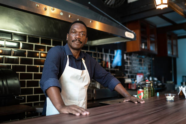 ritratto di un barista serio in piedi dietro il bancone - owner small business restaurant african ethnicity foto e immagini stock