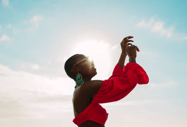 Woman in red dress dancing outdoors on a sunny day Cheerful african woman in red dress dancing outdoors on a sunny day. Female  having fun on the beach with sunshine in background. red dress photos stock pictures, royalty-free photos & images