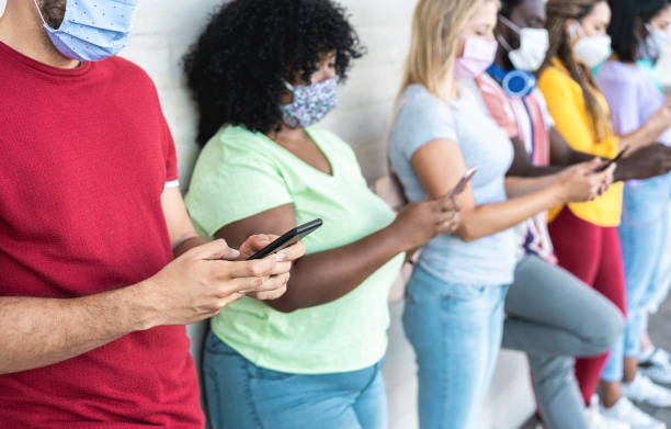 Young people wearing face safety masks using smart mobile phones while keeping social distance during coronavirus time - Technology and covid-19 spread prevention concept - Main focus on first hands los jóvenes que usan máscaras de seguridad faciales usando teléfonos móviles inteligentes mientras mantienen la distancia social durante el tiempo del coronavirus - tecnología y covid-19 difunden el concepto de prevención - enfoque principal en las p