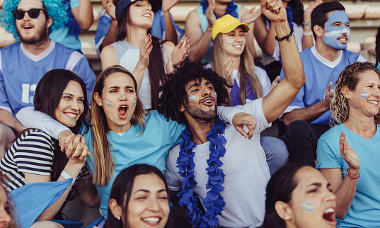 Argentinian spectators in stadium cheering their national football team. People from Argentina in fan zone cheering for their soccer team.