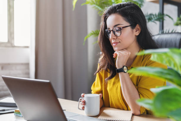 mujer joven disfrutando de su café mientras trabaja o estudia en la computadora portátil en la oficina en casa - tea women cup drinking fotografías e imágenes de stock