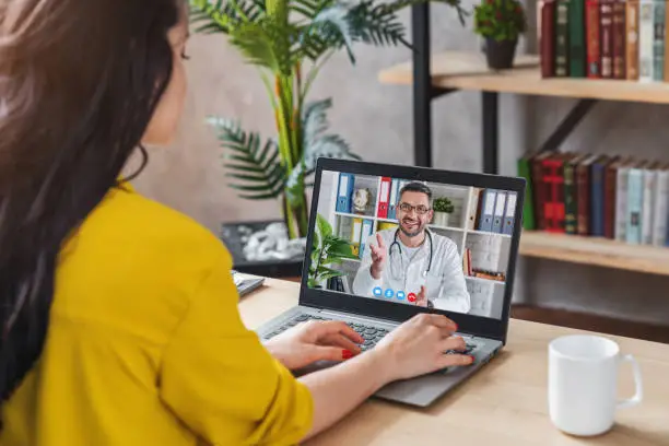 Back view of woman making video call with her doctor while staying at home. Sick girl in online consultation.