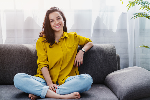 Smiling young woman relaxing while sitting on comfortable couch in living room