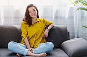 istock Smiling young woman relaxing while sitting on comfortable couch in living room 1254993943