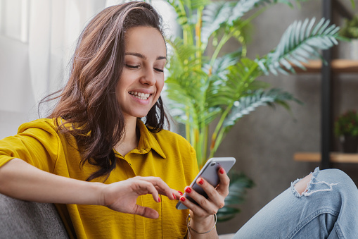 Young woman sitting relax on sofa in living room browsing internet on smartphone