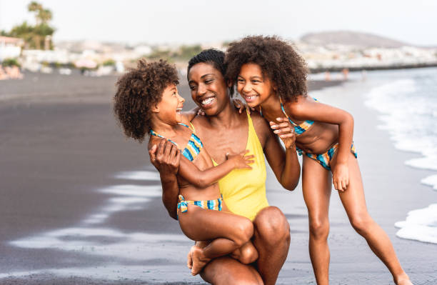 sœurs africaines filles sur la plage avec la mère souriante - les gens de la famille noire s’amuser sur l’heure d’été - vacances, voyage et le concept de style de vie de bonheur - main focus sur le visage de maman - people child twin smiling photos et images de collection