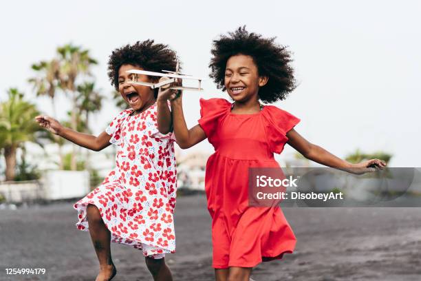 Hermanas Gemelas Afro Corriendo En La Playa Mientras Juegan Con Avión De Juguete De Madera Estilo De Vida Juvenil Y Concepto De Viaje Enfoque Principal En La Cara Correcta Del Niño Foto de stock y más banco de imágenes de Niño