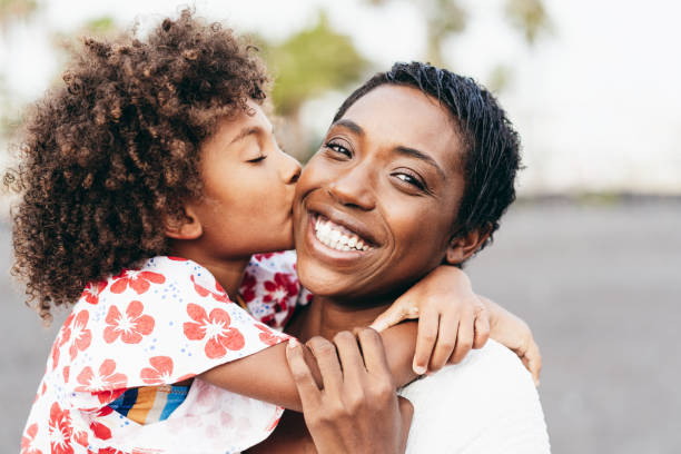 feliz joven madre divirtiéndose con su hijo en el día de verano - hija besando a su madre al aire libre - estilo de vida familiar, maternidad, amor y momentos tiernos concepto - enfoque en la cara de la mujer - family single mother black mother fotografías e imágenes de stock