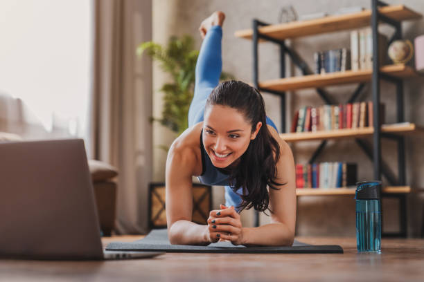 istock Fit woman doing yoga plank and watching online tutorials on laptop while training in living room at home 1254996086