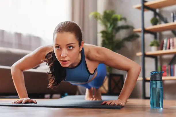 Beautiful young sports lady doing push ups while workout at home