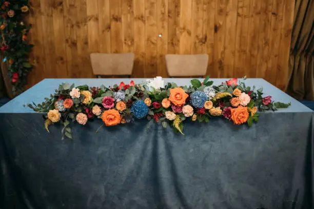 Wedding presidium in restaurant, free space. Wedding banquet table for newlyweds with flowers, greenery, blue velvet. Lush floral arrangement on wedding table