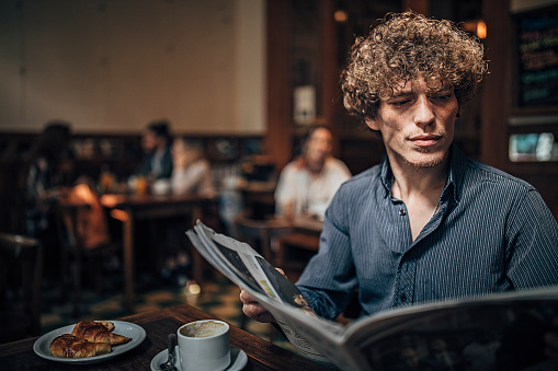 One man, man on coffee break in city cafe, reading newspaper.