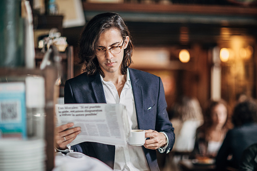 Group of people, man on coffee break in city cafe, reading newspaper.