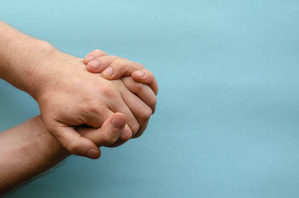 Interlocked fingers of two male hands on blue background. Hands of an adult of Caucasian ethnicity. Series of hand gestures. View from above. Copy space. Selective focus.