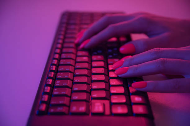 istock Woman with orange manicure working on wireless keyboard in neon light. 1255005394
