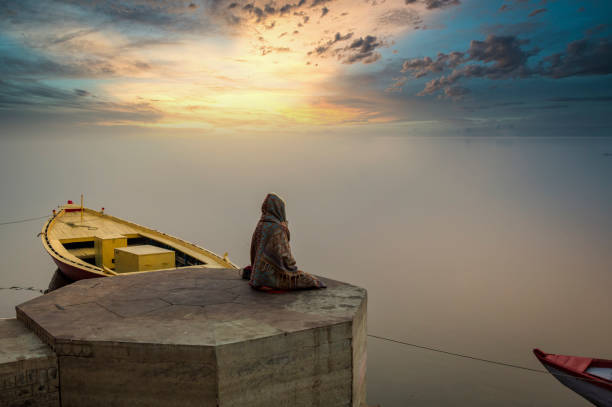 une personne médite sur la rive du ganga de fleuve sur les ghats de varanasi tandis que le soleil se lève - india ganges river indian culture varanasi photos et images de collection