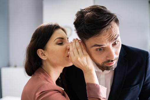 Woman Whispering Gossip In Friend's Ear At Workplace In Office