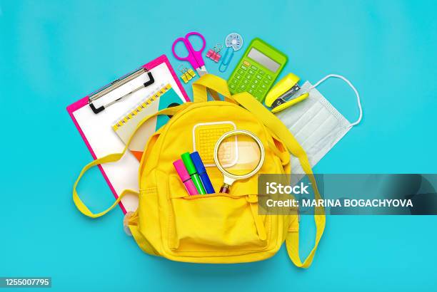 Back To School Education Concept Yellow Backpack With School Supplies Protective Medical Mask Calculator Scissors Isolated On Blue Background Top View Copy Space Flat Lay Stock Photo - Download Image Now