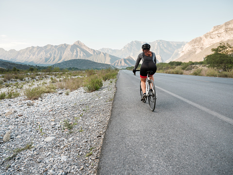 Back view of a latin woman cycling on the road with mountains  in the backgound.