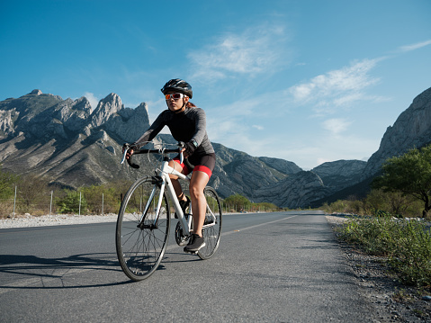 Beautiful scenery of mountains in the background and a female cyclist cycling on the road.