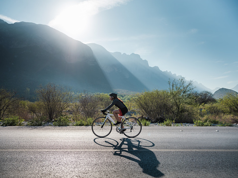 A latin cyclist cycling on the  road and the sun setting on the mountains.