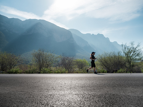 A young latin woman running outside on the road in a beautiful day with mountains in the background.