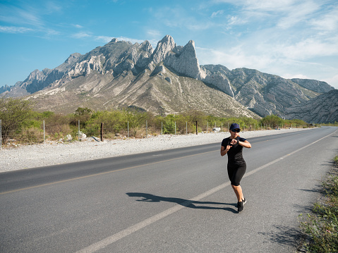 A young latin woman running outside on the road and looking at her watch.