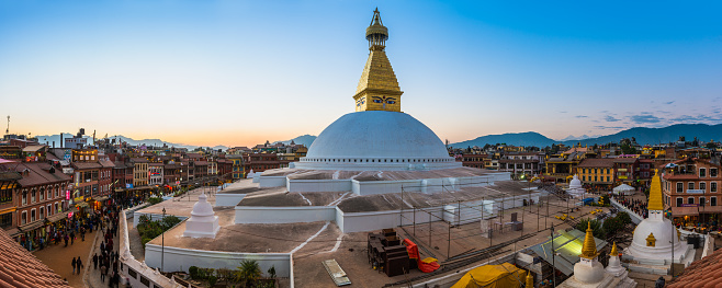 The iconic mandala dome of Boudhanath stupa, spotlit beneath dramatic sunset skies as crowds of pilgrims and tourists walk around the ancient Buddhist shrine, a UNESCO World Heritage Site in Kathmandu, Nepal's vibrant capital city.