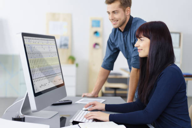 Two business colleagues checking a spreadsheet Two successful hardworking young business colleagues checking a spreadsheet together on a desktop monitor with pleased smiles, man and woman spreadsheet photos stock pictures, royalty-free photos & images