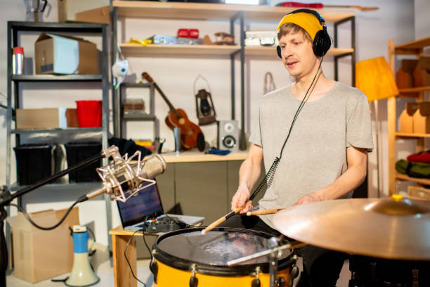 istock Young drummer with headphones beating drum with drumsticks during rehearsal 1255012477