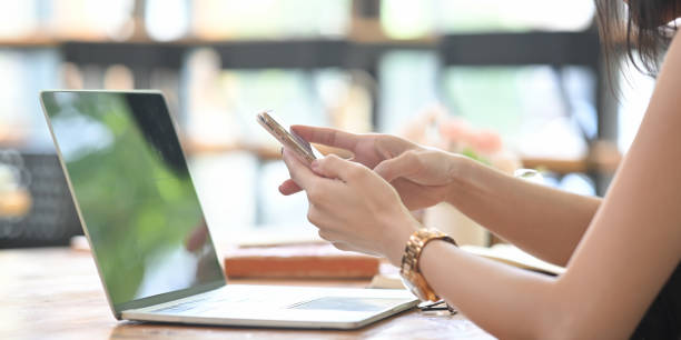 istock Cropped image of a woman is using a smartphone while sitting in front of a computer laptop. 1255012822
