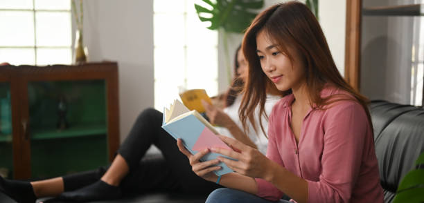istock Young Asian women are reading a book while sitting together on a black leather sofa. 1255012901