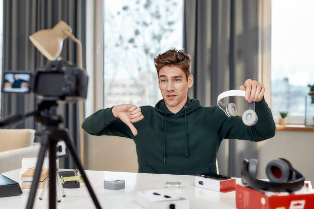 istock Its not worth it. Young male technology blogger showing thumbs down after testing new headphones, while recording video blog or vlog review at home studio. Blogging, Work from Home concept 1255016923