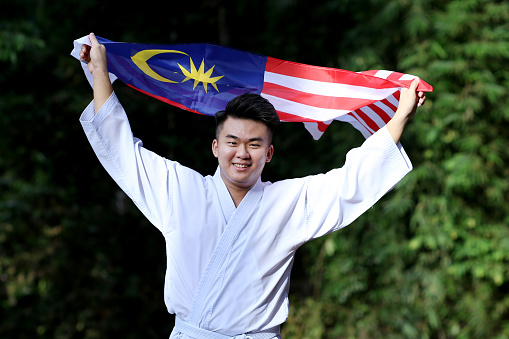 A young man waving Malaysian flag joyfully at nature reserve in Malaysia.