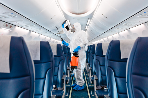 Men in protective suits and masks disinfecting airplane. Unrecognizable person.