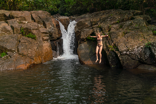 Cool tropical vacations. Mature woman jumping into the water from a waterfall.