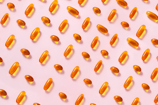 Abundance of yellow fish oil capsules repetition on soft pink background