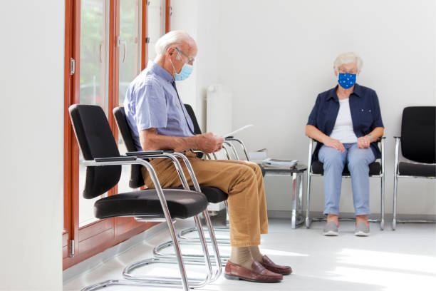 Senior woman and man sitting with face masks in a bright waiting room of  a hospital or an office Senior woman and man sitting with face masks in a bright waiting room of  a hospital or an office medical office lobby stock pictures, royalty-free photos & images