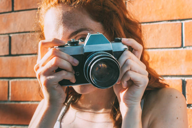 joven sostiene una cámara analógica y mira a través del visor - single lense reflex fotografías e imágenes de stock