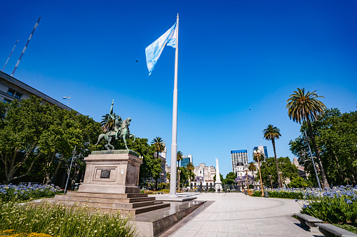 The Equestrian monument to General Manuel Belgrano, a landmark of Buenos Aires, and the Argentinian Flag in Buenos Aires, Argentina. It is located at Plaza de Mayo, in front of the Casa Rosada.