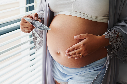 Cropped shot of an unrecognizable woman touching her pregnant belly and holding a sonogram