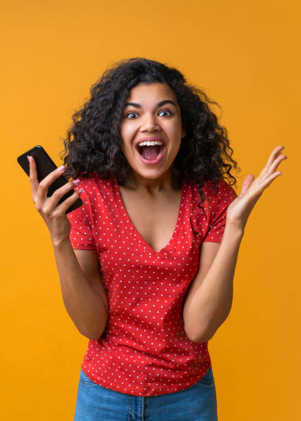 vertical shot of amazed girl with mobile phone in hands celebrating victory in online casino, hitting jackpot in lotttery, making bets online at bookmaker's website - smiling casino human hand beautiful imagens e fotografias de stock