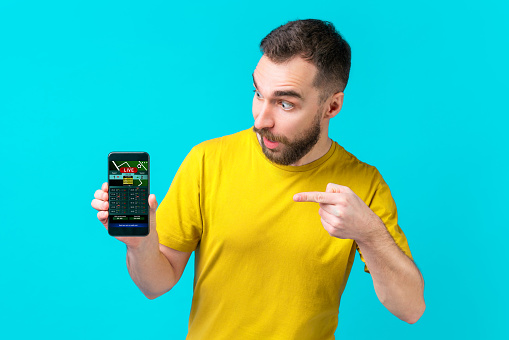 Surprised football fan pointing with his index finger at the smartphone screen with bookmaker's website interface template. Gambling, sport betting, money win concept.