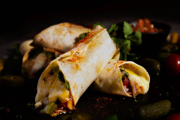 mexican burritos with paprika on top with pickled cucumber, tomato, cheese, garlic, bell pepper, jalapeno and black pepper background served with mexican tomato sauce - mexico chili pepper bell pepper pepper imagens e fotografias de stock